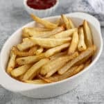 Oven baked fries in a white dish next to a small bowl of ketchup.