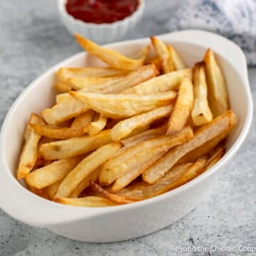 Oven baked fries in a white dish next to a small bowl of ketchup.