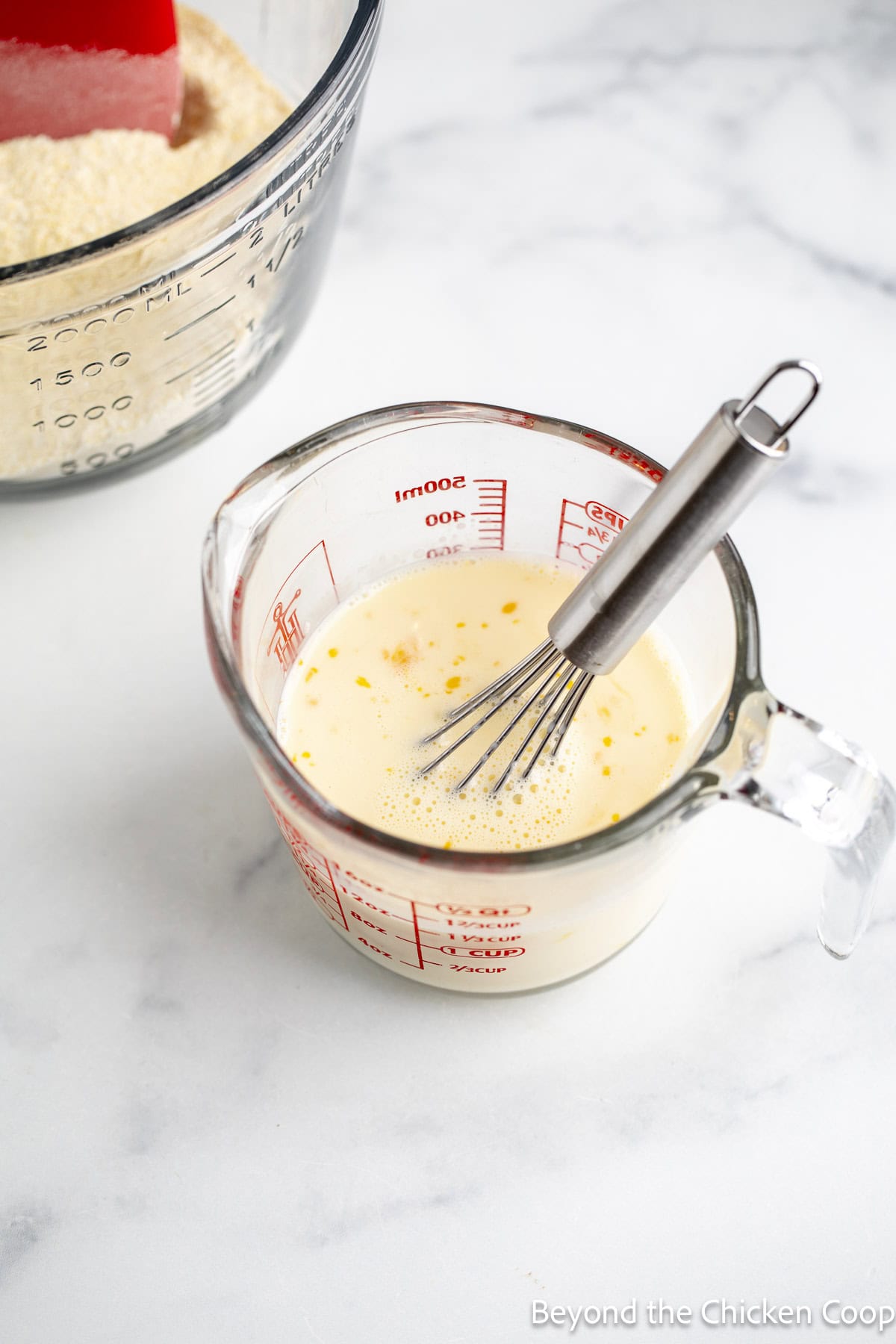 Milk, egg, and butter in a glass measuring cup with a whisk.