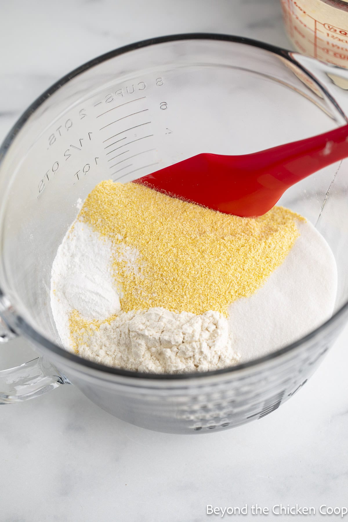 Flour, cornmeal, sugar, and baking powder in a glass bowl.