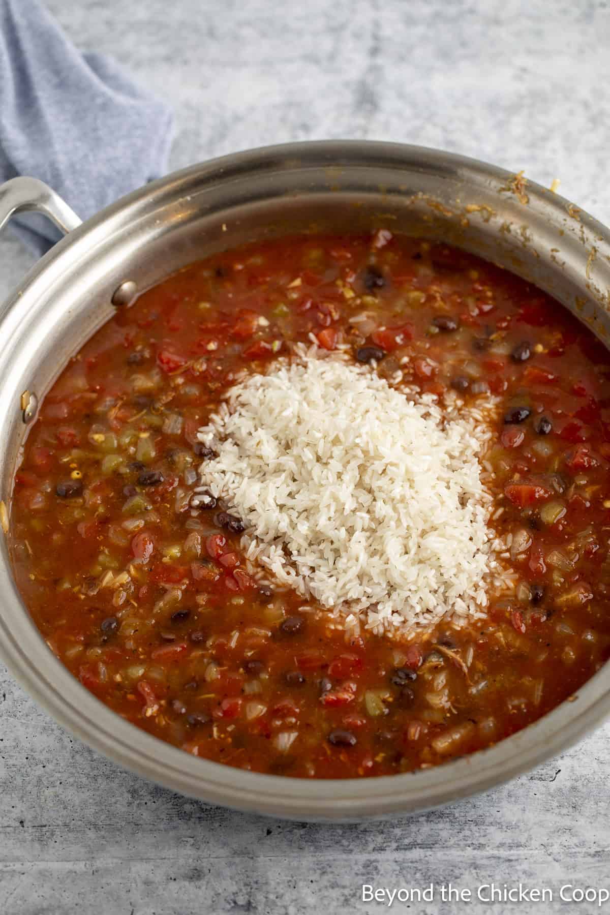 Uncooked rice added to a skillet filled with a red sauce.