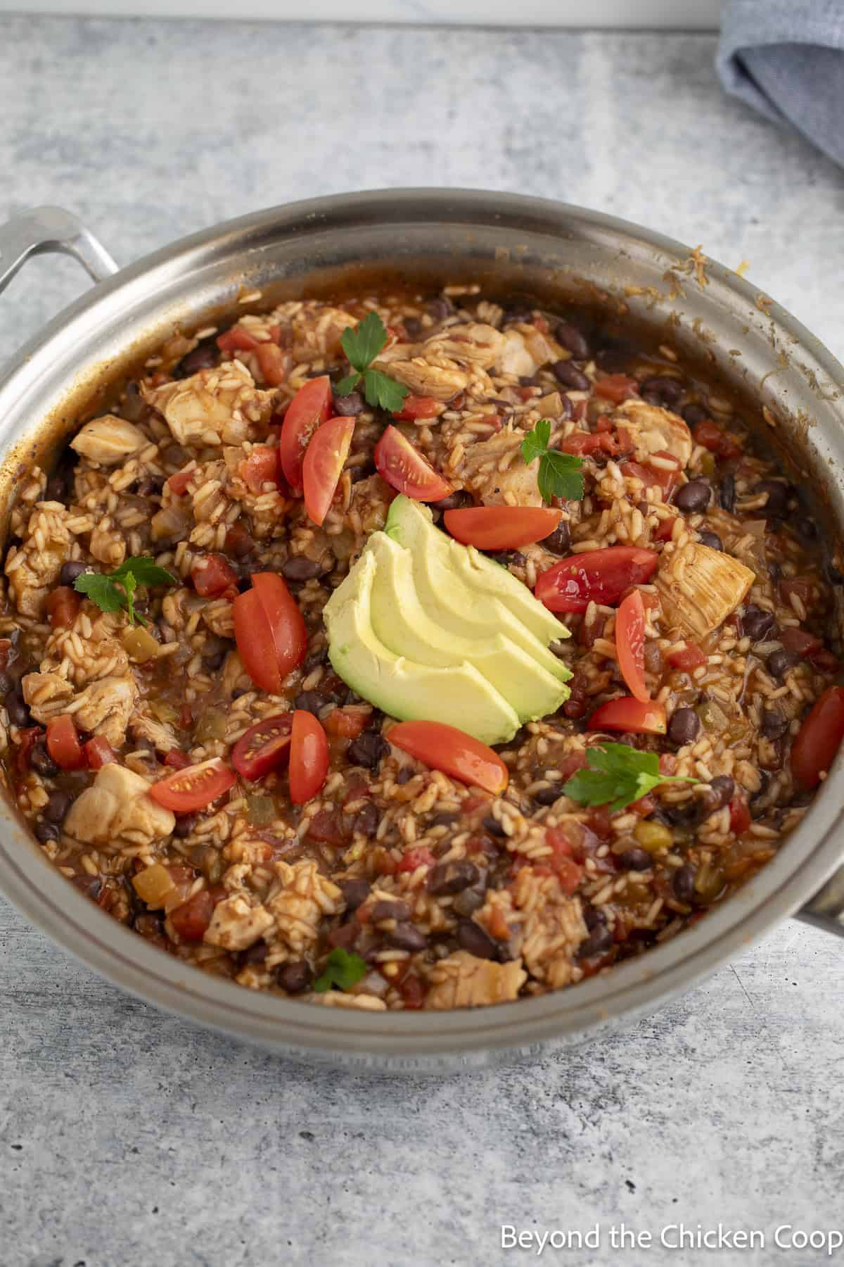A chicken skillet dish in a pan topped with chopped tomatoes and a sliced avocado.