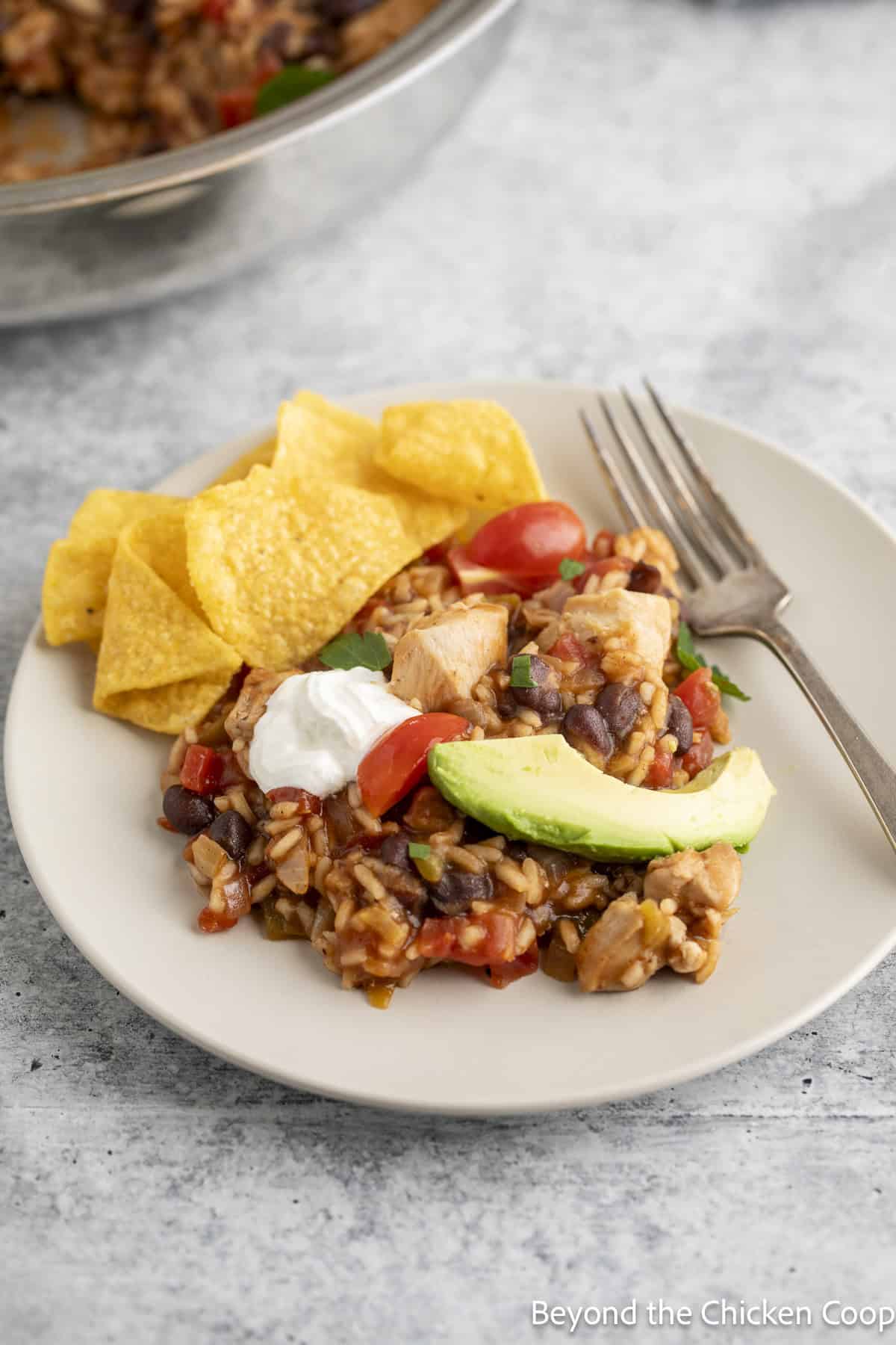 A rice dish with black beans topped with an avocado slice, tomatoes, and sour cream.