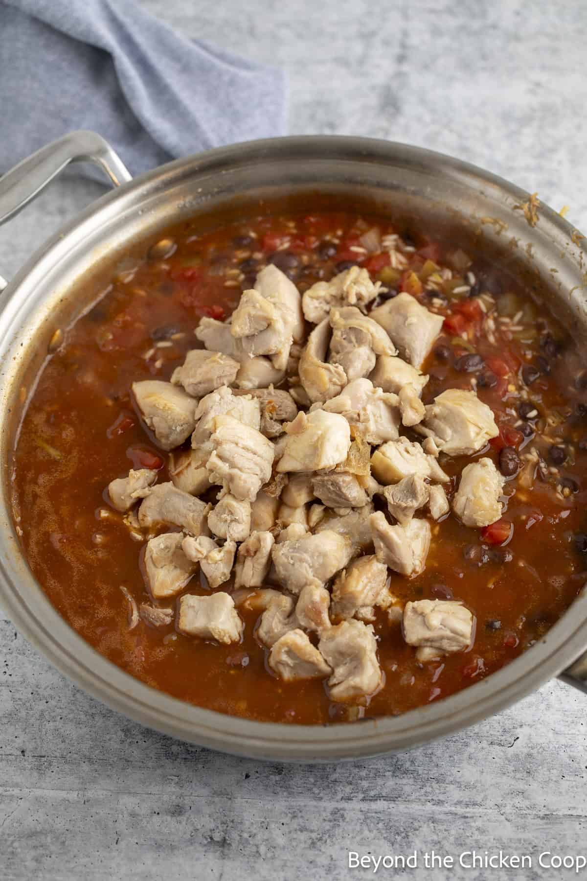 Cubed chicken in a pan with enchilada sauce.