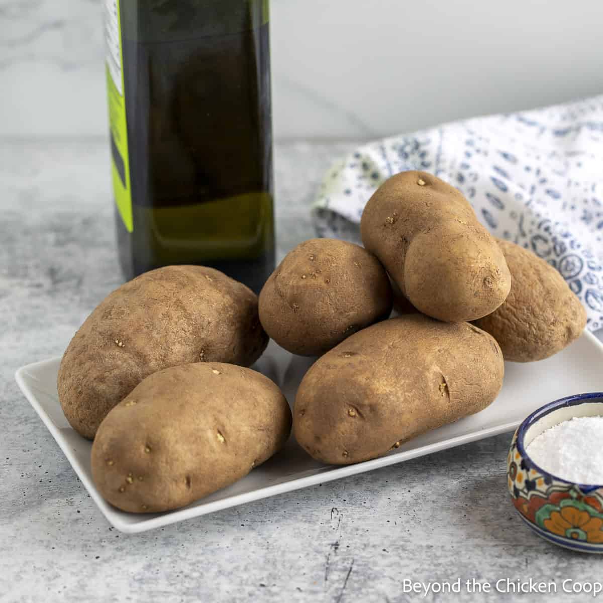 A plate with russet potatoes, a small bowl of salt, and a bottle of oil.