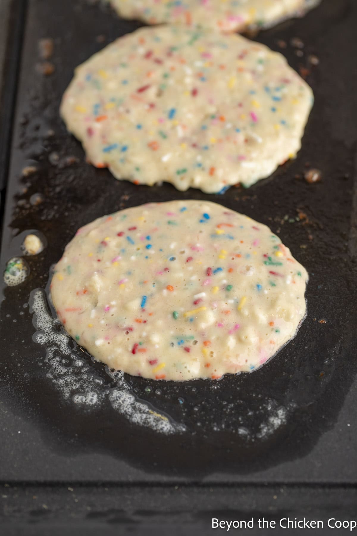 Pancakes with sprinkles cooking on a skillet.