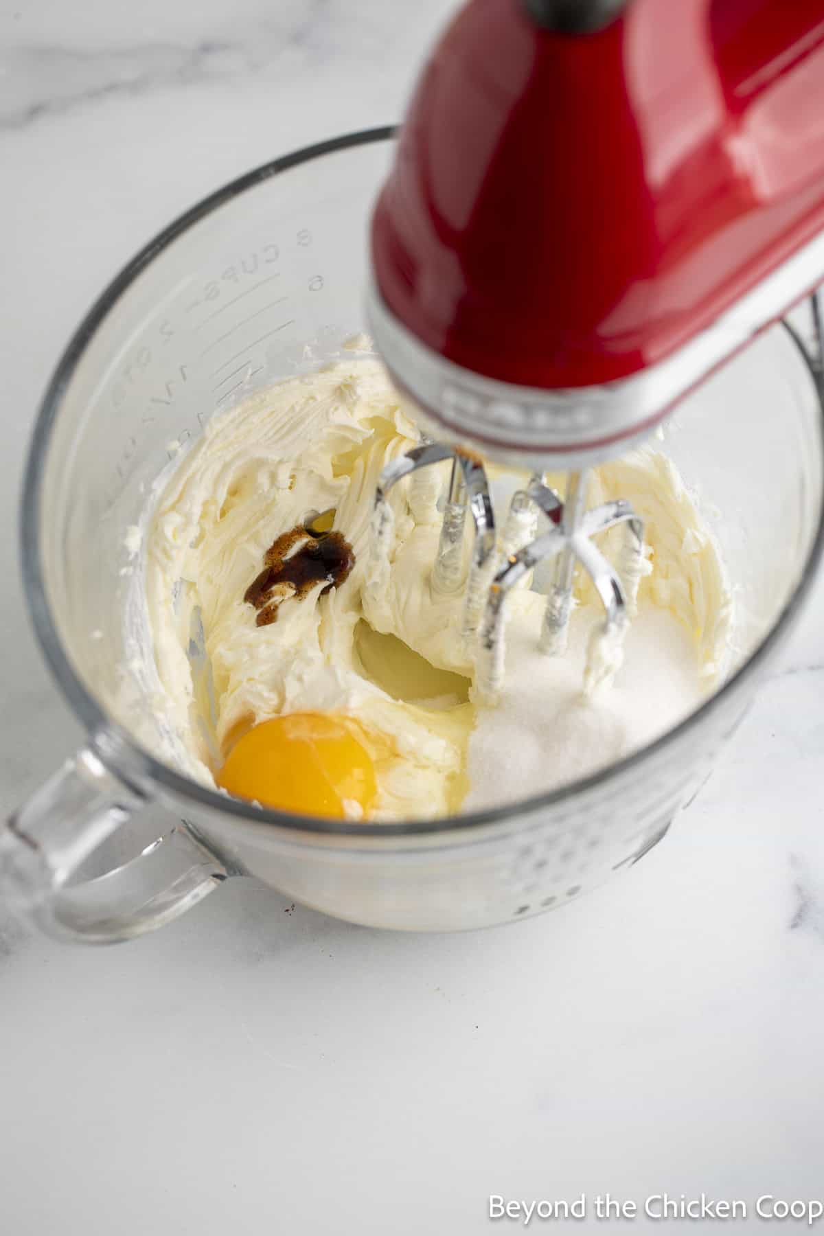 Mixing an egg, sugar, and vanilla into cream cheese.