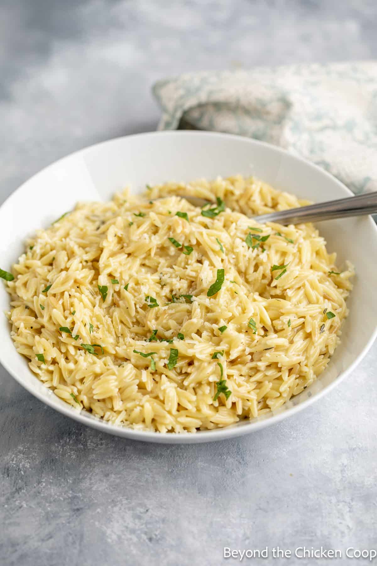 Orzo pasta topped with chopped parsley in a white bowl with a spoon.
