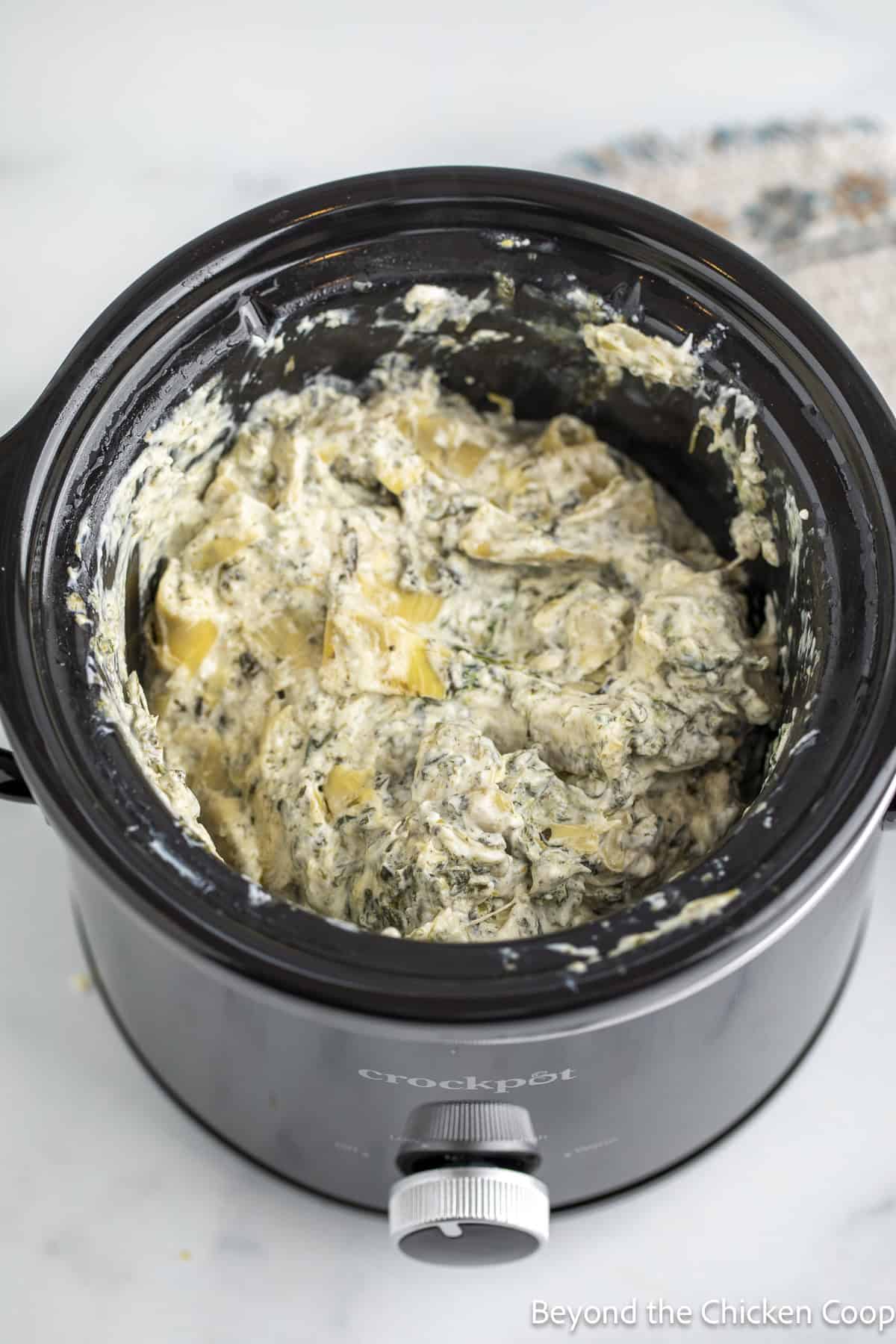 Creamy dip with artichokes and spinach in a crock pot.