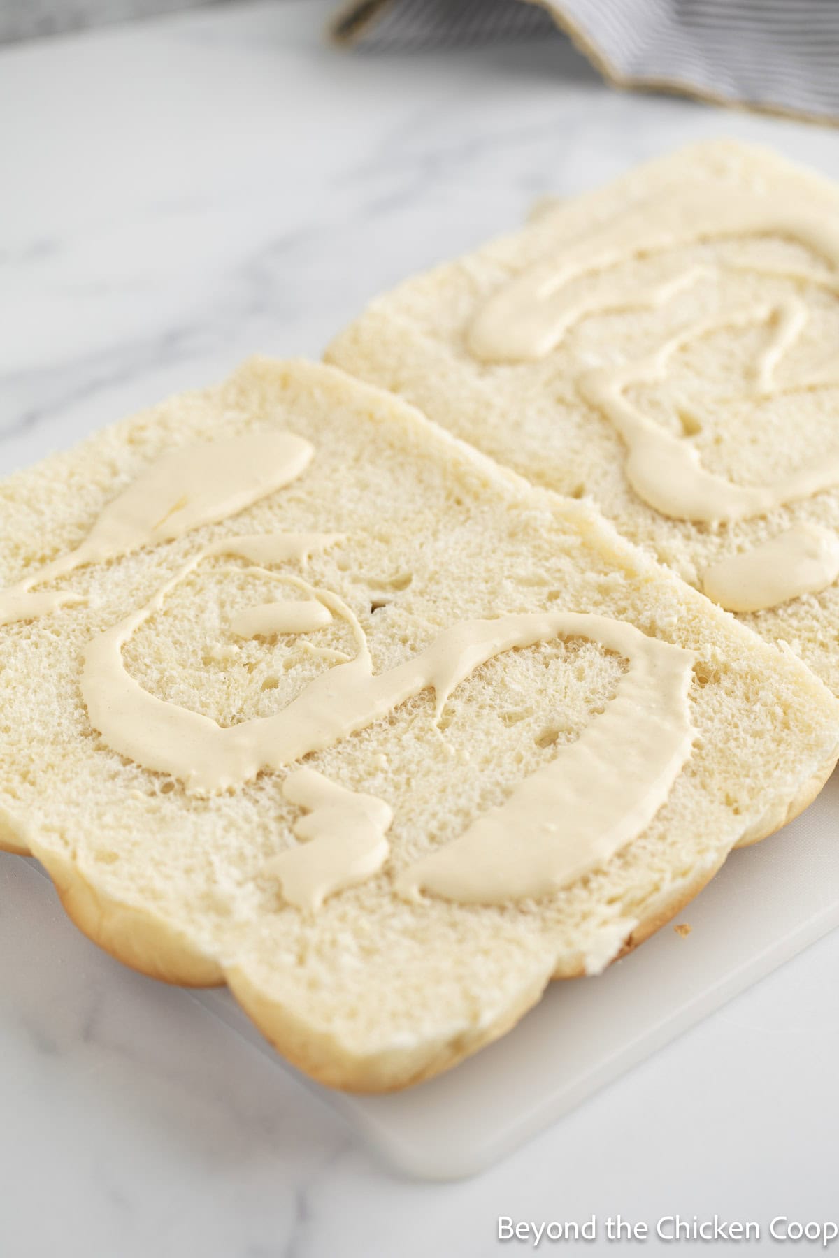 Slider rolls cut in half and topped with mayonnaise.