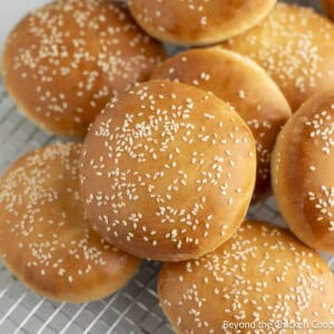 Homemade Hamburger Buns with sesame seeds stacked on a baking rack.
