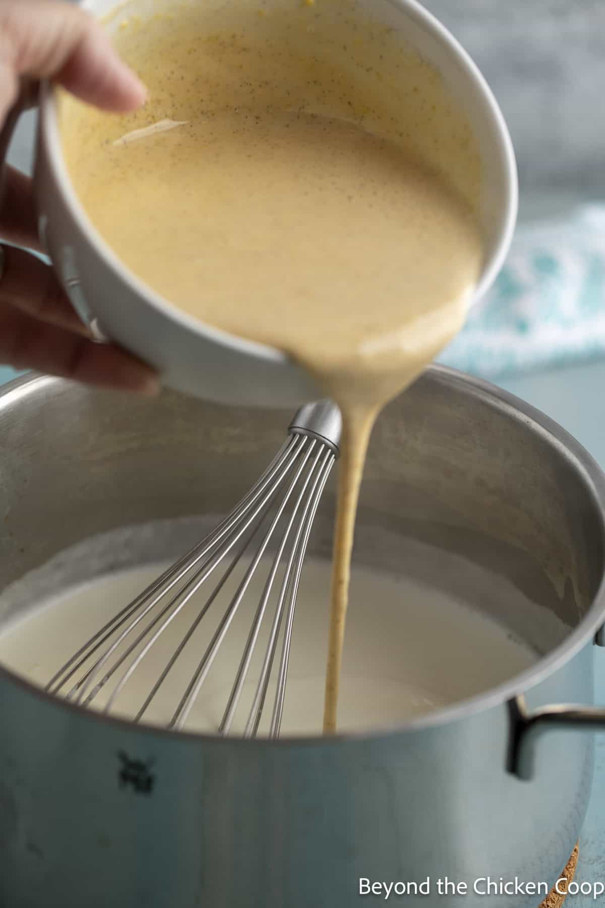 Whisking egg yolks into warm milk in a pot.