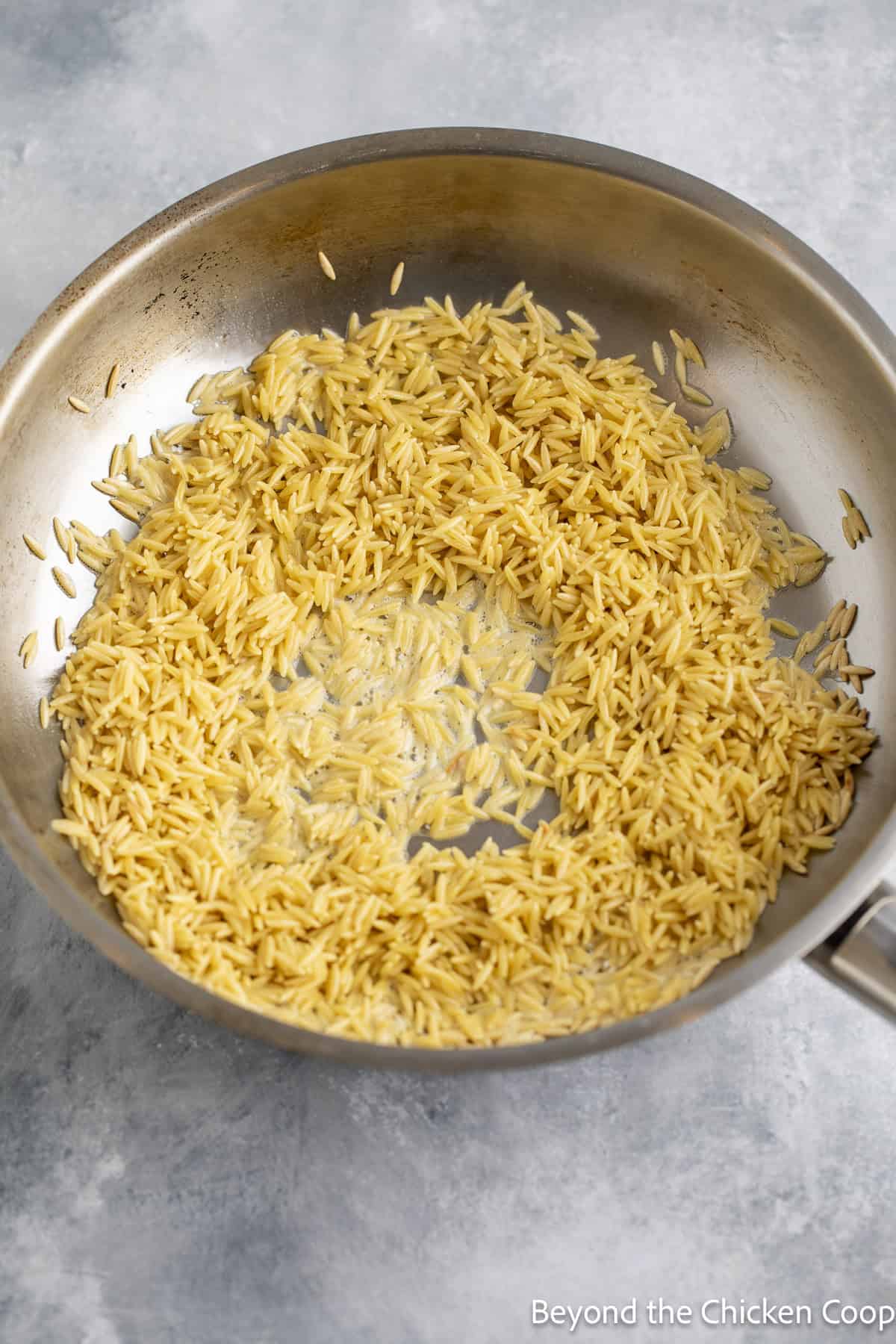 Uncooked orzo in a skillet with butter.