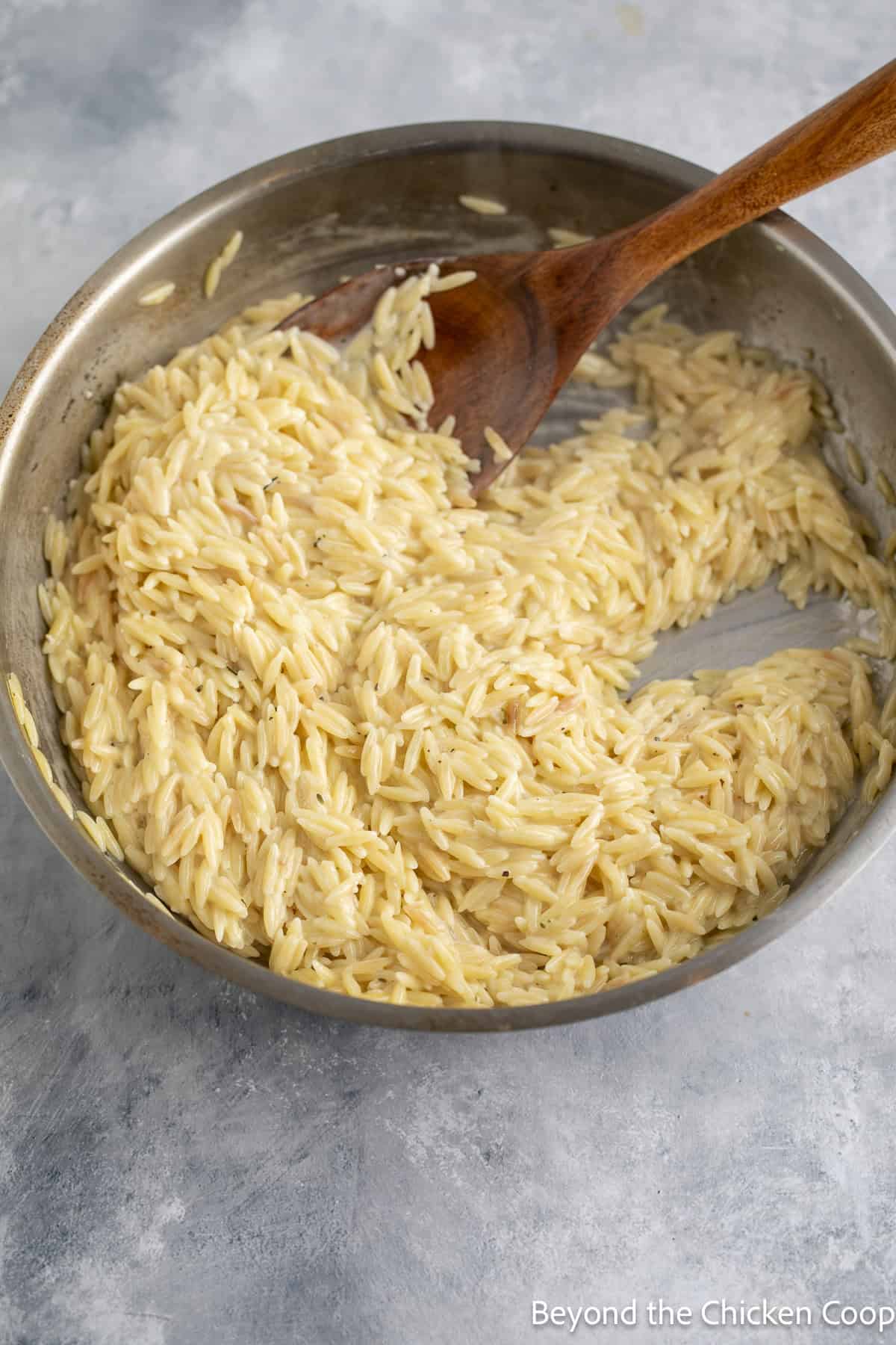 Creamy pasta in a skillet with a wooden spoon.