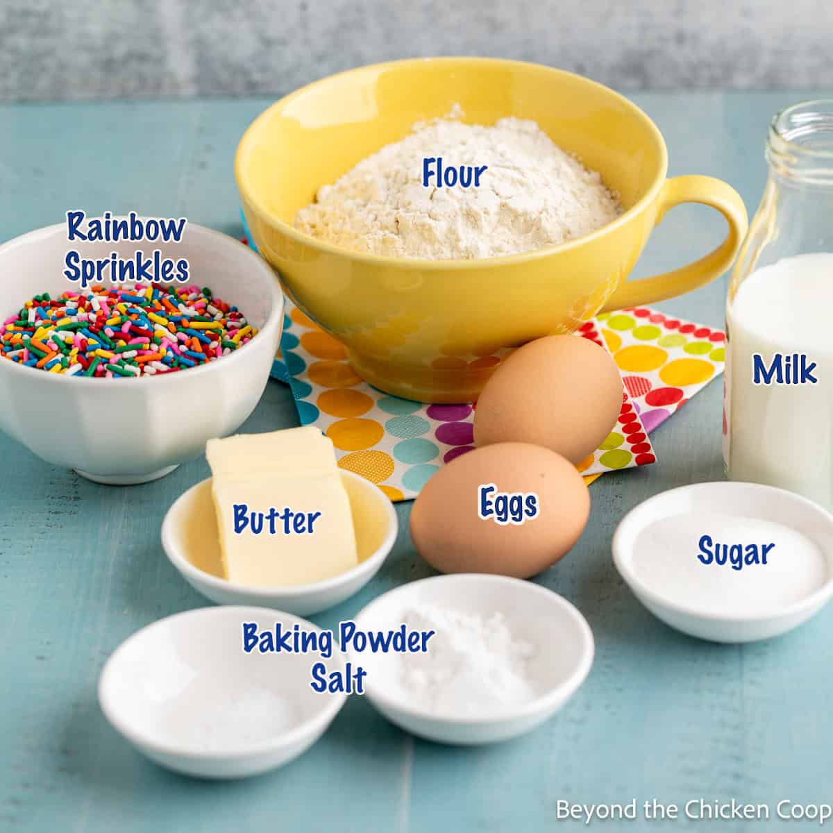 Small bowls filled with flour, sugar, butter, and colored sprinkles.