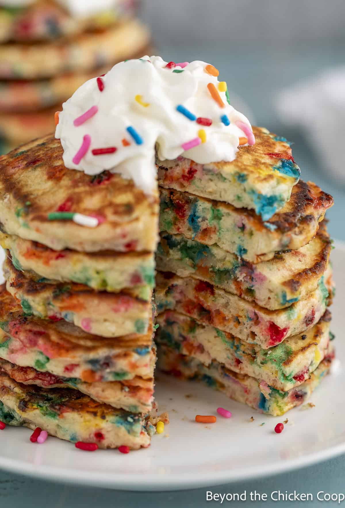 A stack of rainbow sprinkle pancakes with a wedge cut out of one side of the stack.