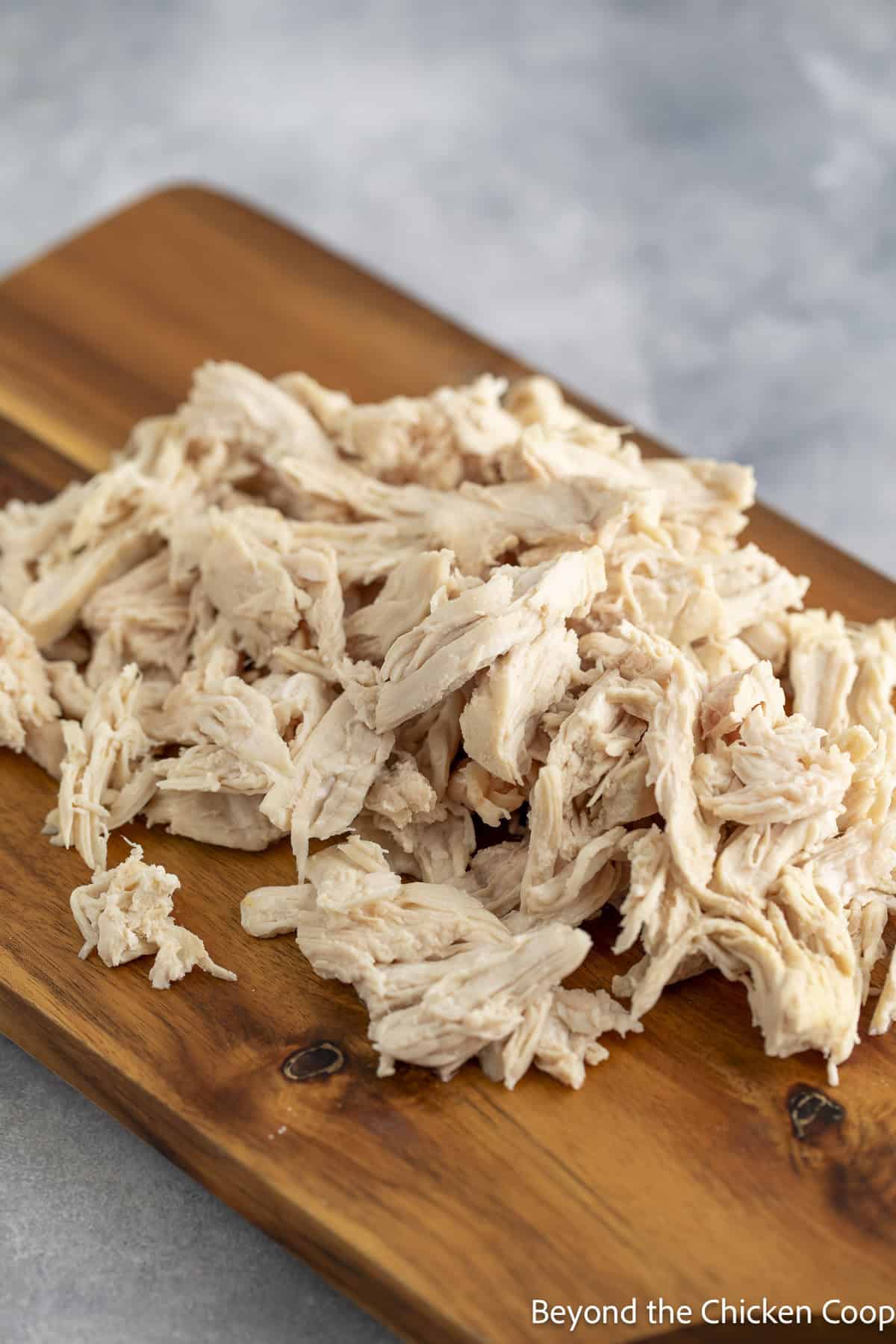 A pile of shredded chicken on a wooden cutting board.