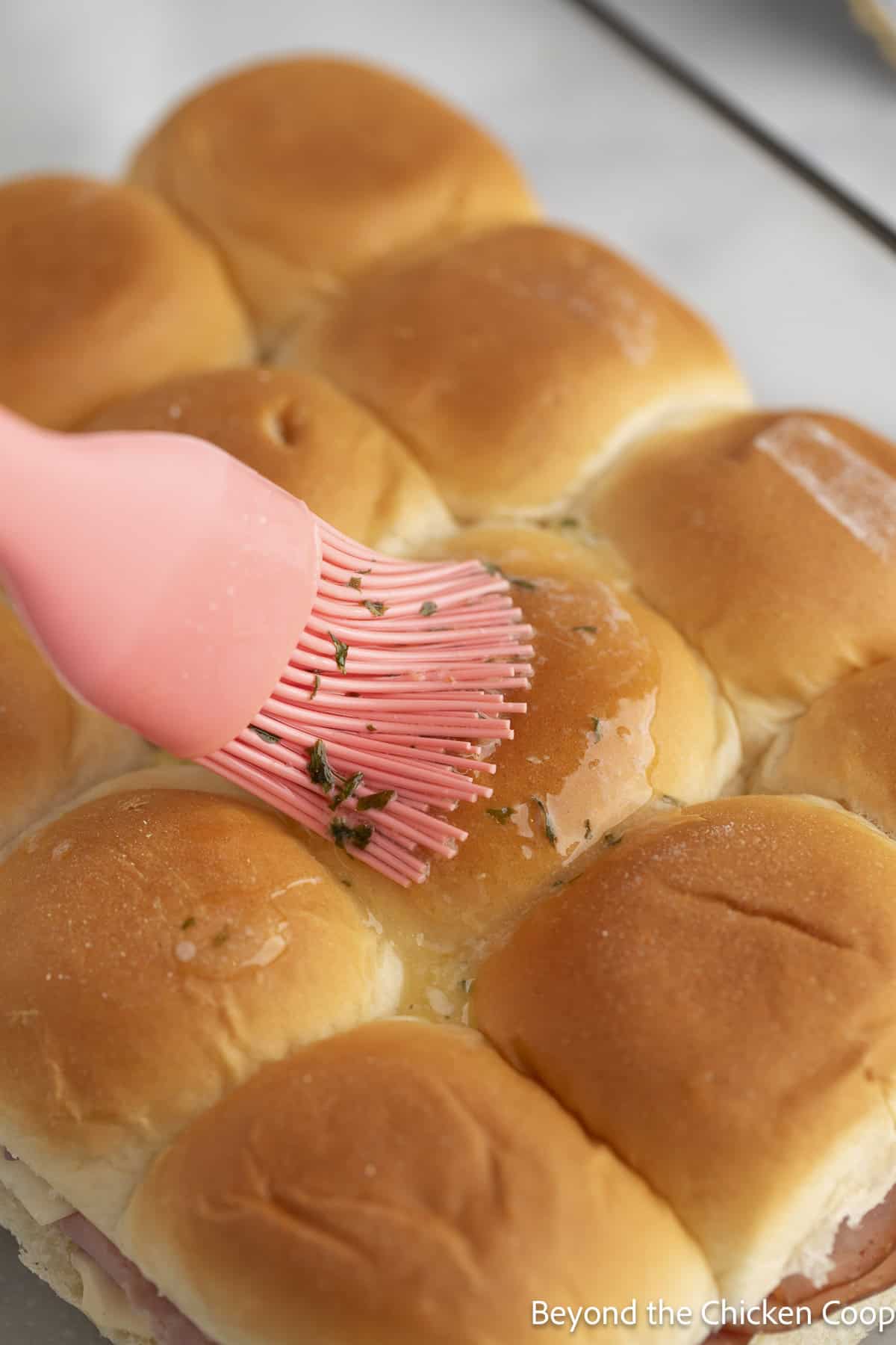 Brushing butter on the top of rolls.