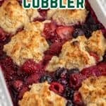 A berry cobbler topped with biscuits in a white casserole dish.