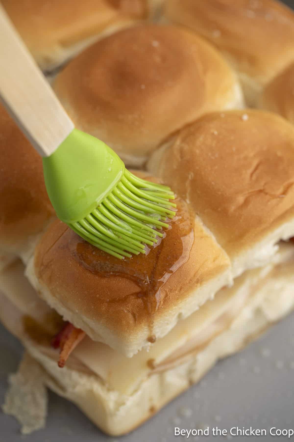 Brushing butter over the top of slider buns.