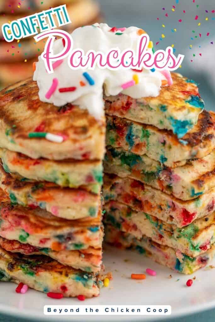 A stack of rainbow sprinkle pancakes topped with whipped cream.