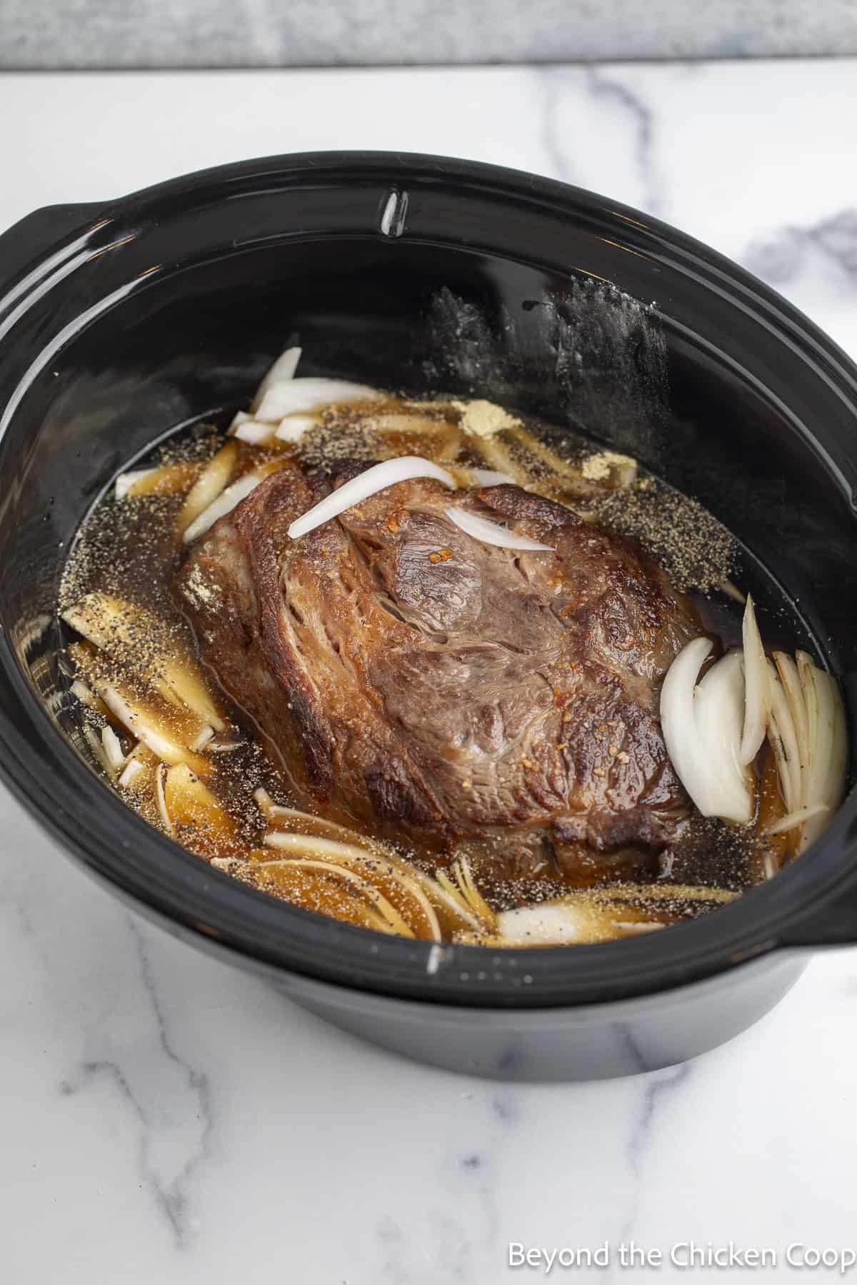A beef roast with onions in a crock pot.