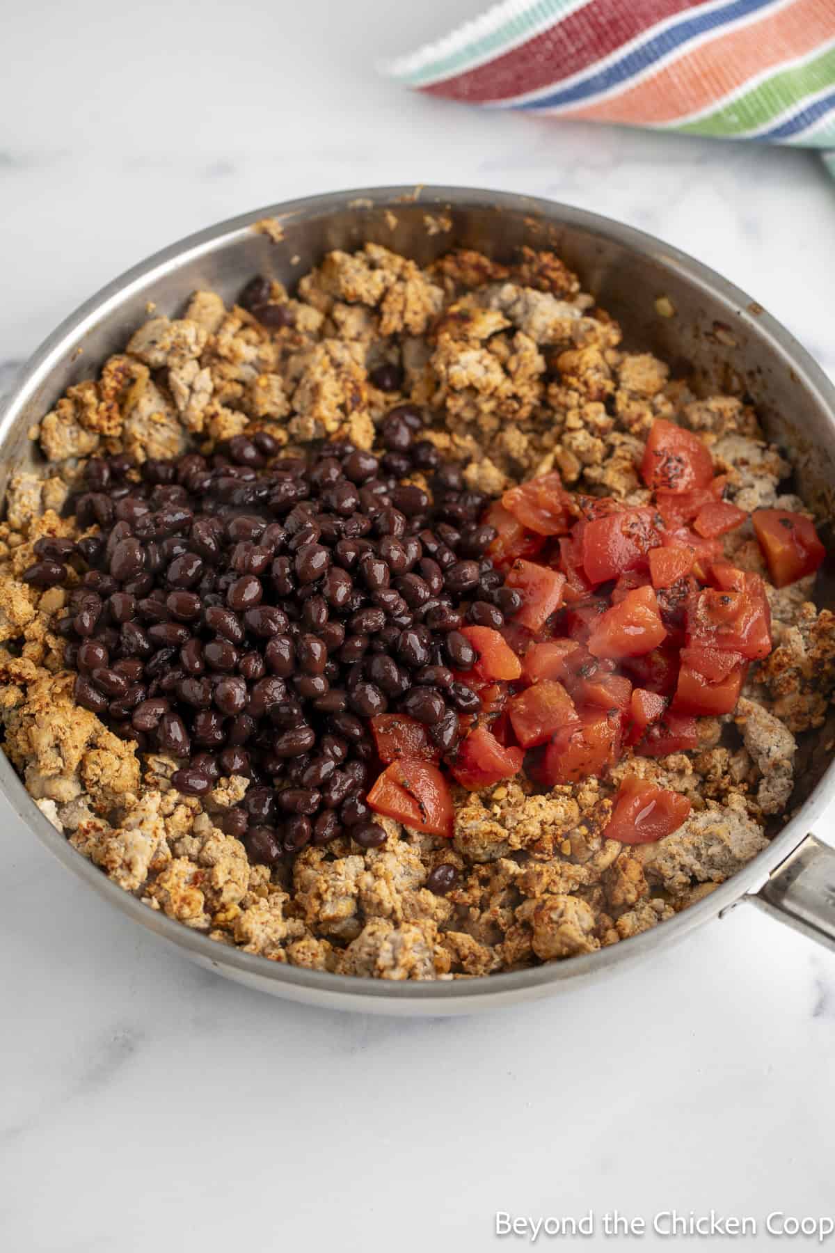 Cooked ground turkey in a skillet with black beans and tomatoes.