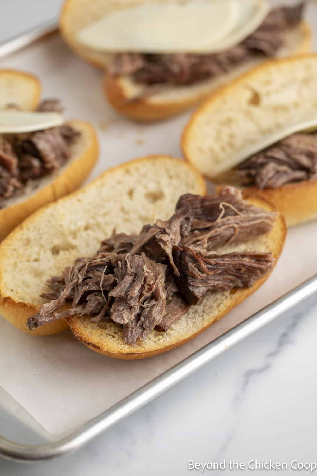 A sheet pan with toasted buns topped with shredded beef.