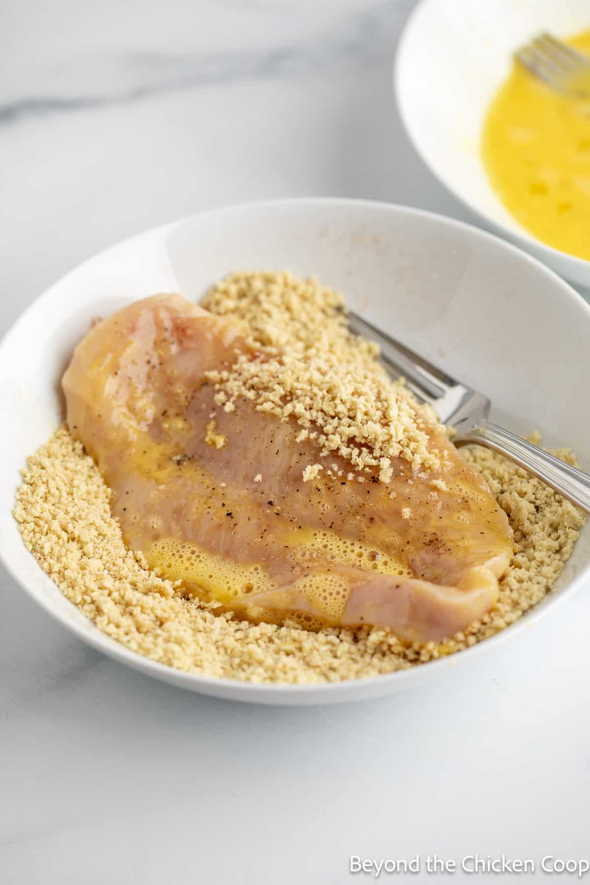 A chicken cutlet in a bowl filled with breadcrumbs.