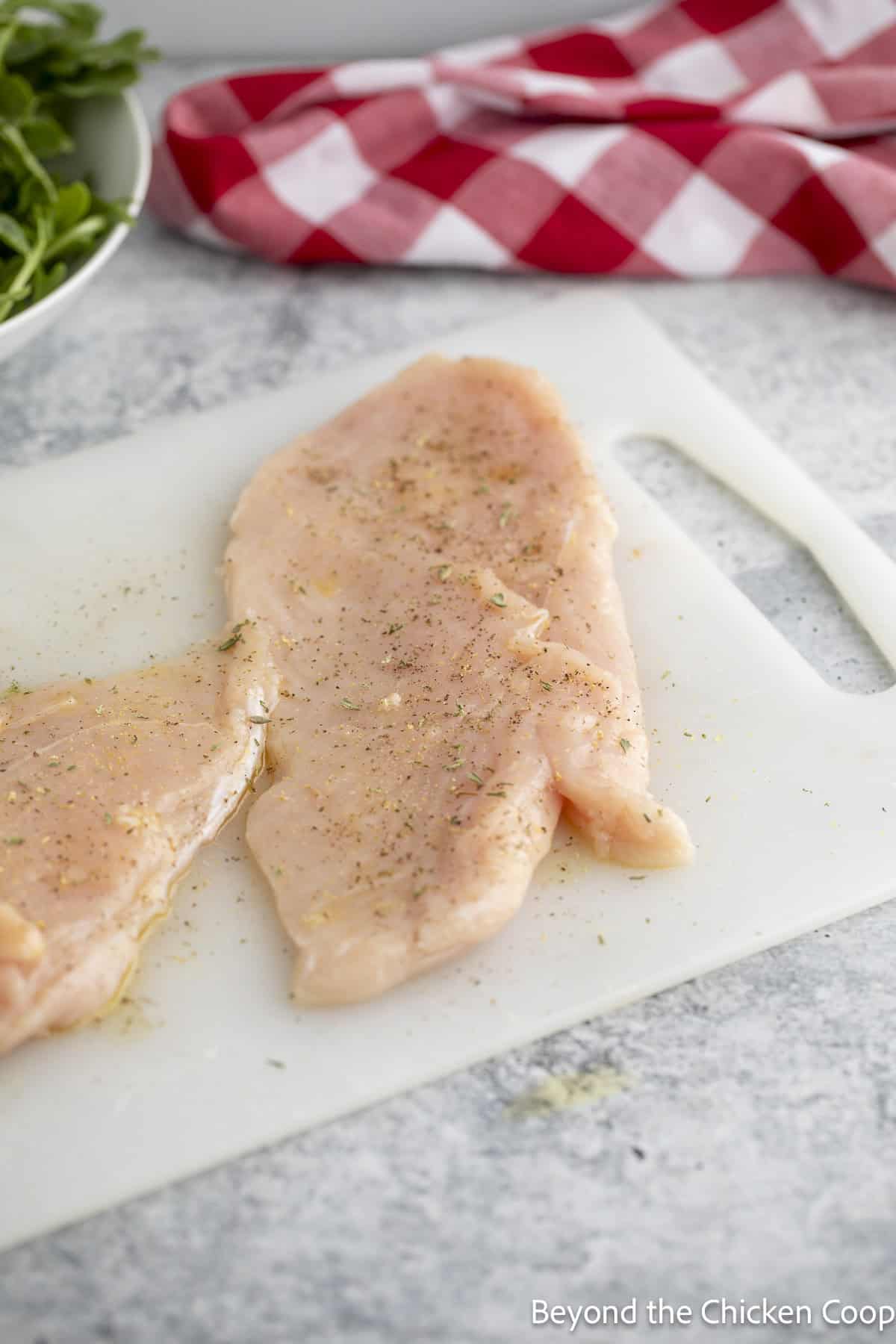 Seasoned chicken breasts on a cutting board.