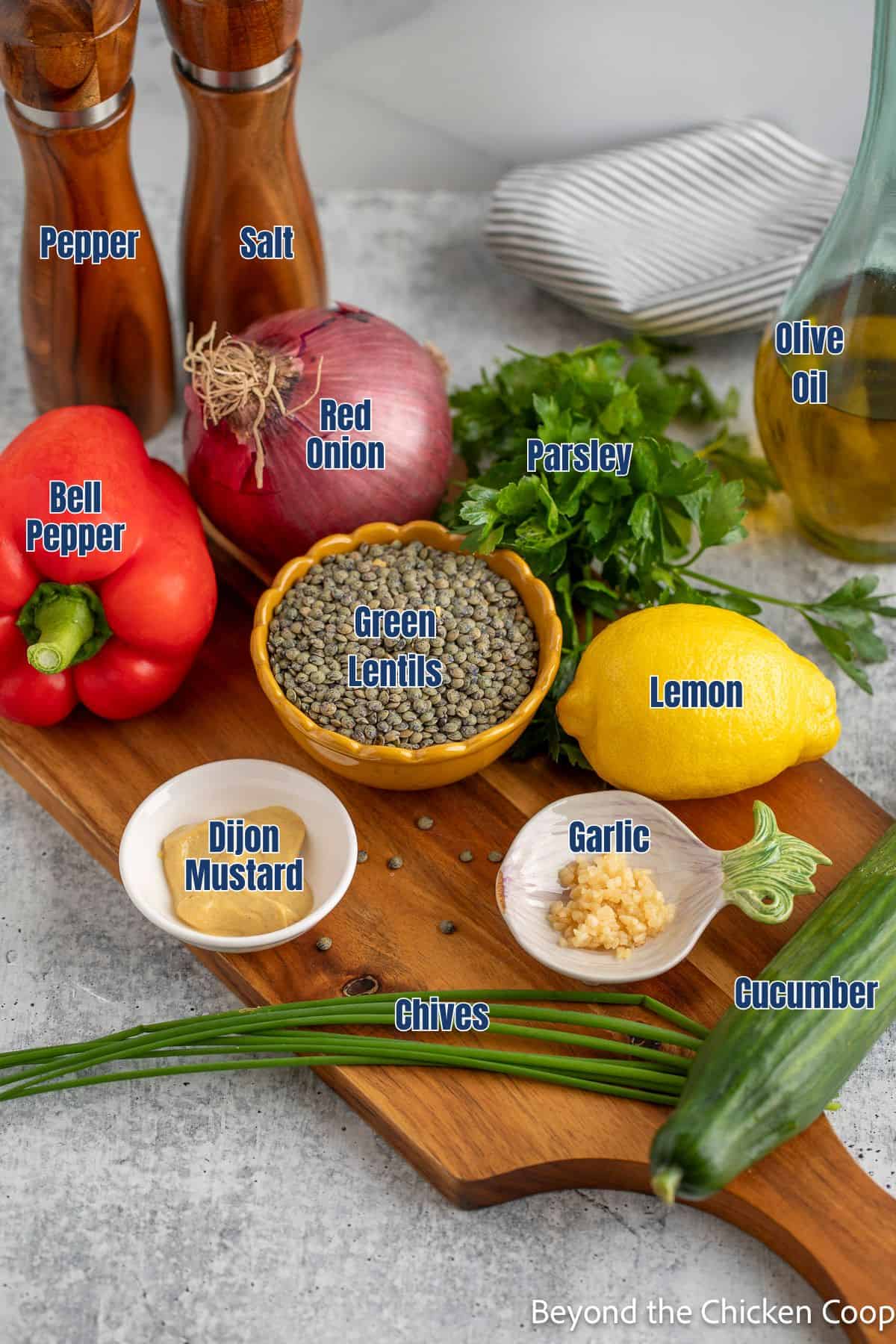 A small bowl with green lentils next to fresh veggies, herbs, and a lemon.
