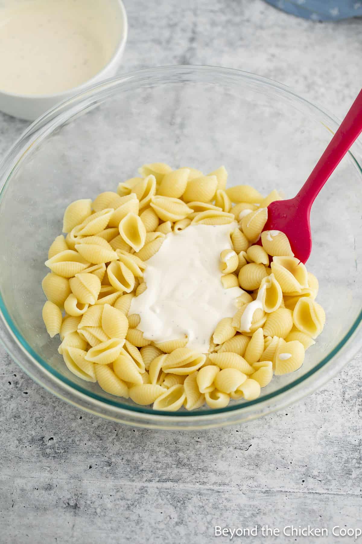 Mixing a dressing with cooked pasta in a large glass bowl.