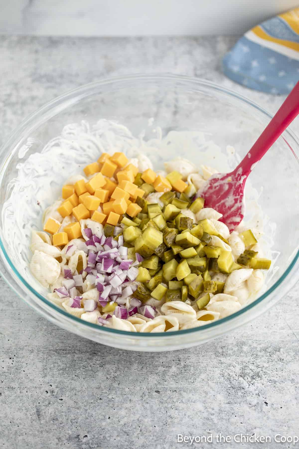 Chopped pickles, cheese, and onions added to a bowl of pasta.