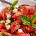 Tomato wedges, fresh basil, and small mozzarella balls mixed together in a bowl.