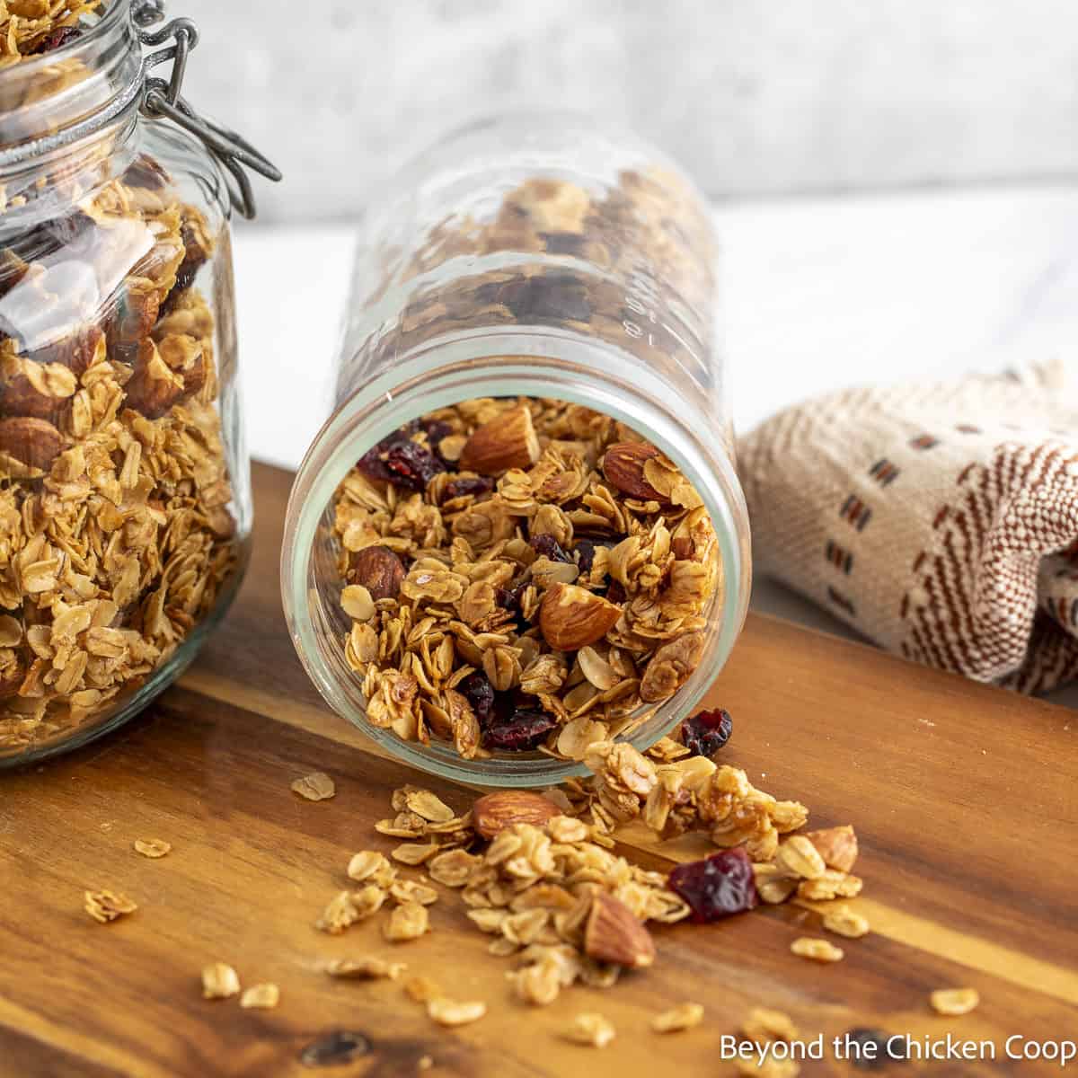 Granola spilled out of a jar onto a wooden board.