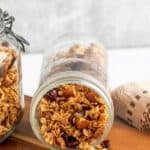 Granola spilling out of a glass jar onto a wooden board.