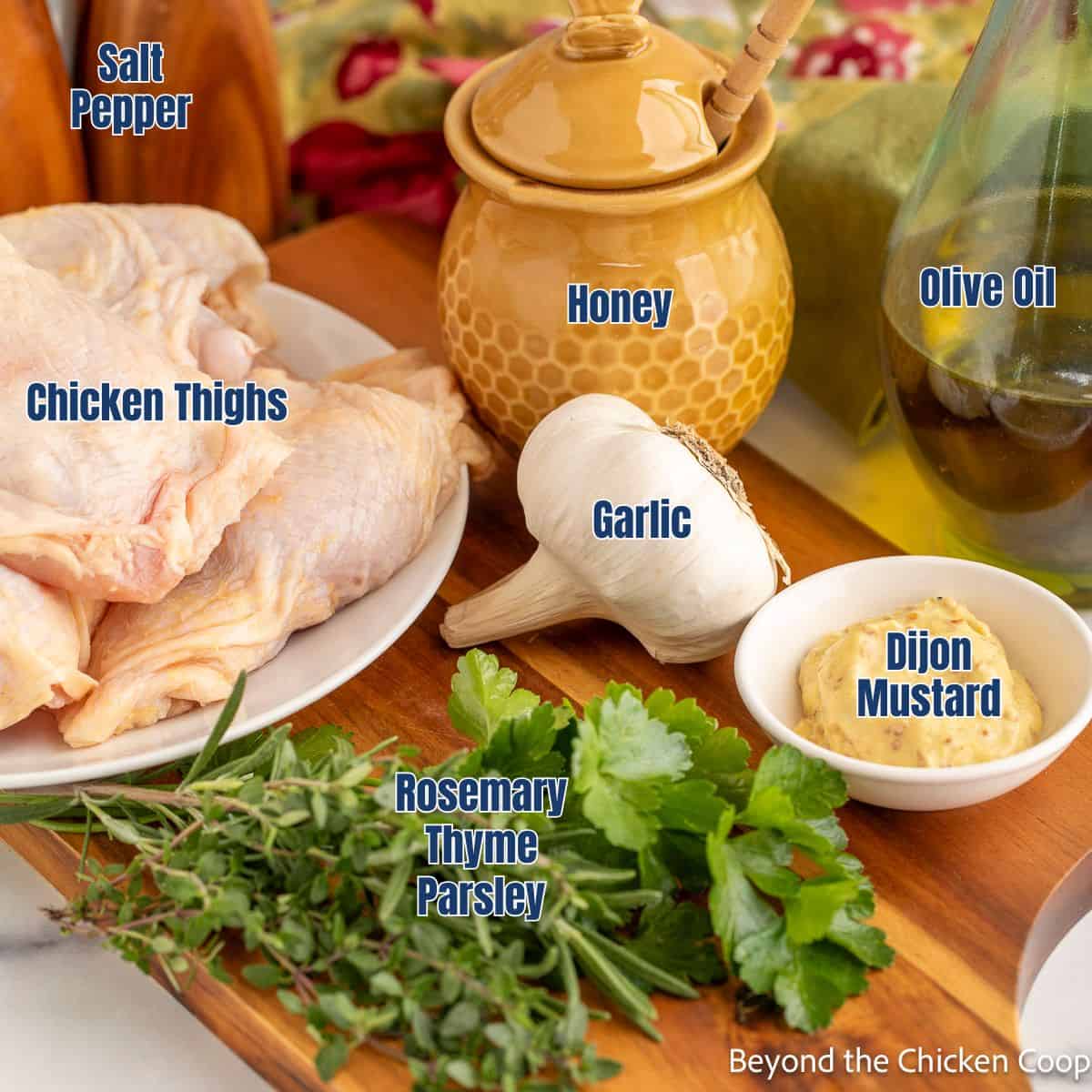 Chicken thighs, fresh herbs, garlic, honey, and mustard displayed on a wooden board.
