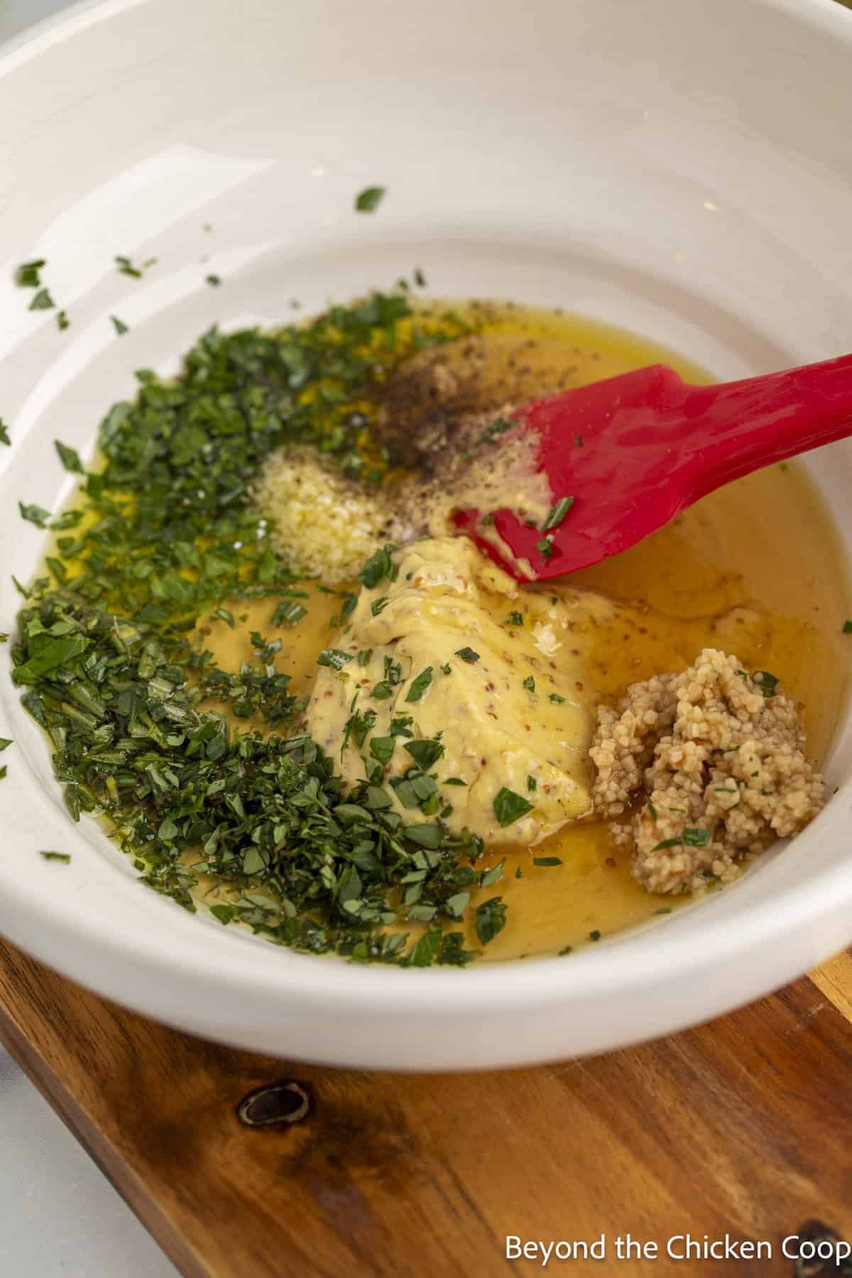 A bowl with oil, honey, mustard, garlic and fresh herbs.