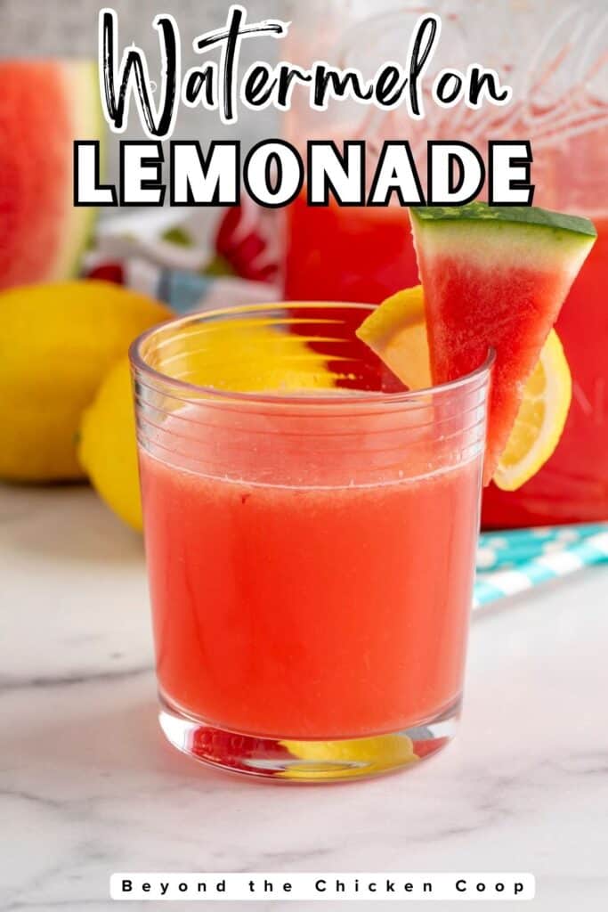 A glass filled with pink lemonade with a watermelon wedge on the rim of the glass.