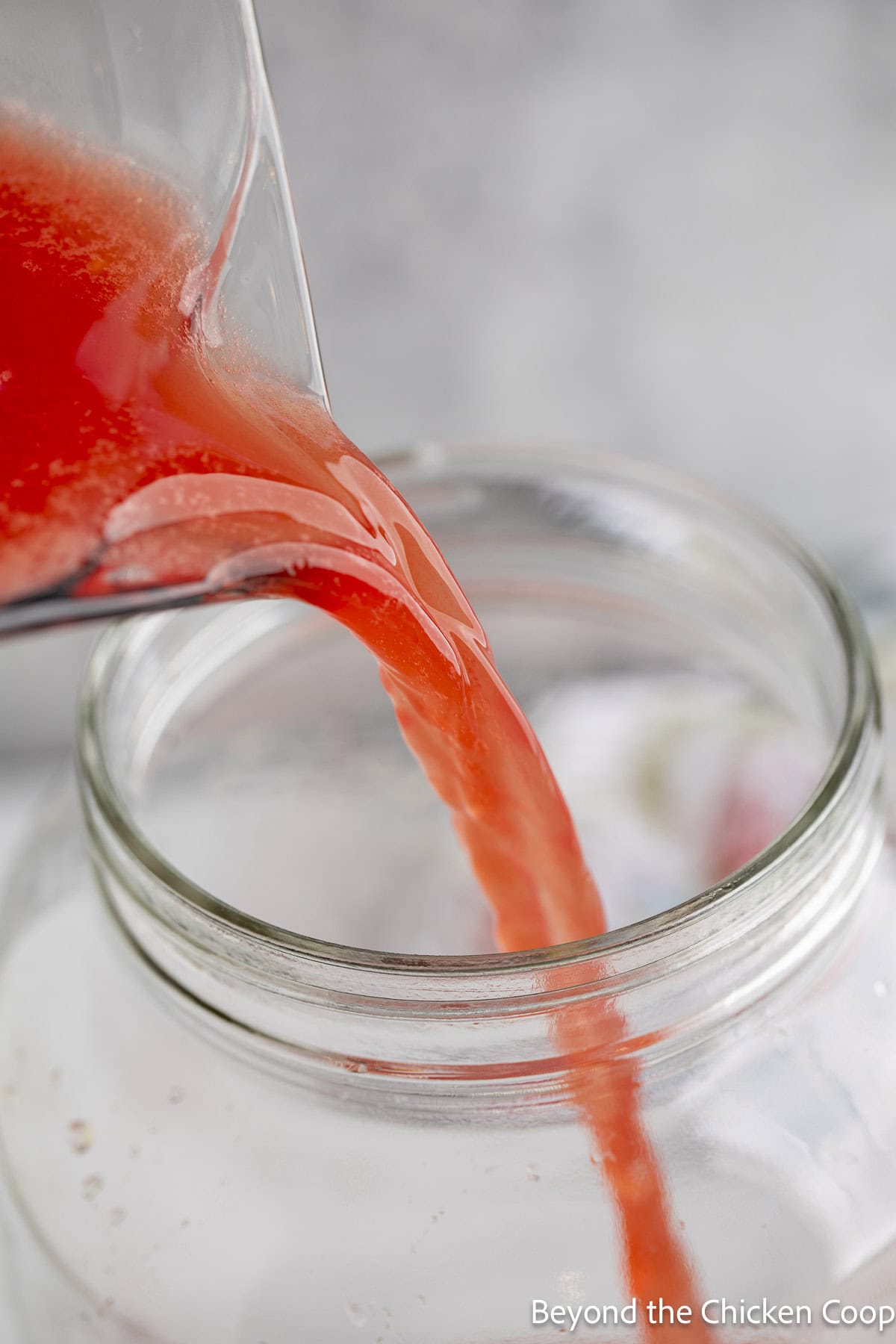 Pouring watermelon juice into a glass jar.