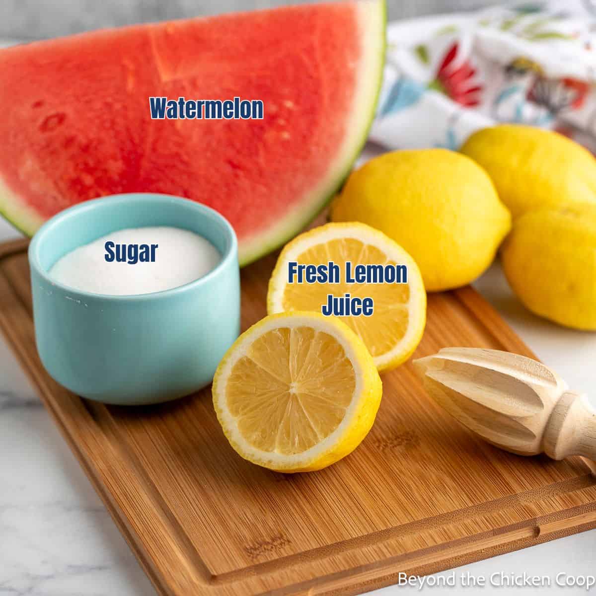 Fresh lemons, a watermelon wedge, and a small bowl of sugar on a wooden board.