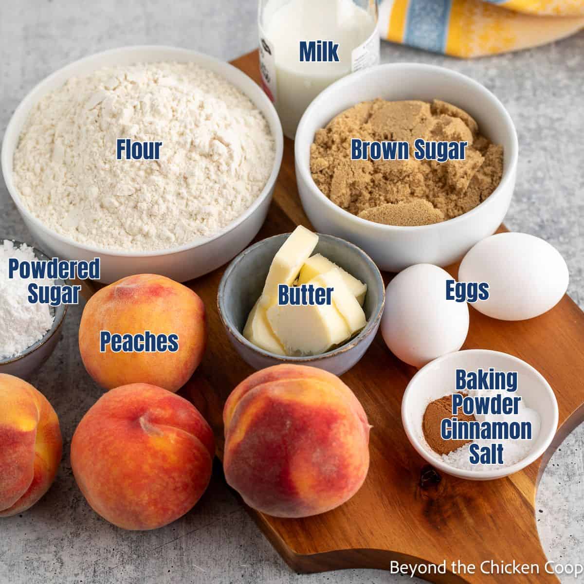 Fresh peaches, bowls of flour, sugar, and butter on a wooden board.