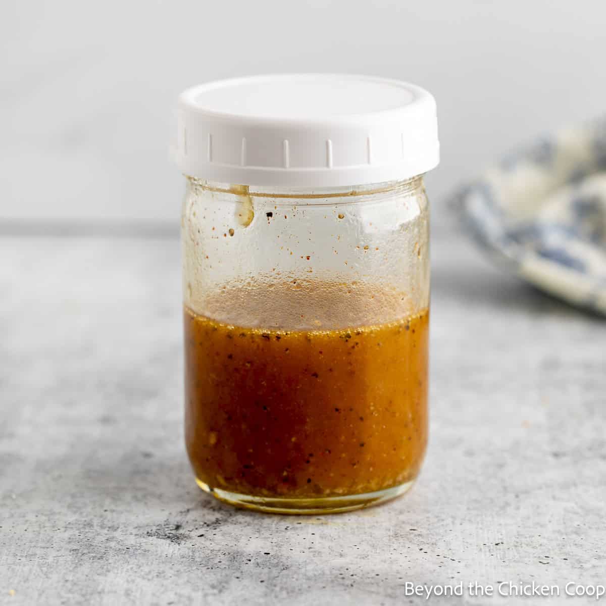 A glass jar filled with a vinaigrette dressing.