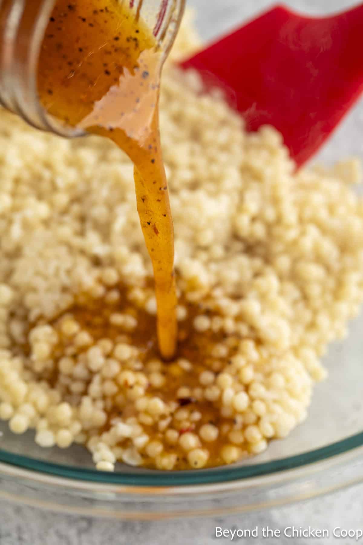 Pouring a vinaigrette over cooked pearl couscous.