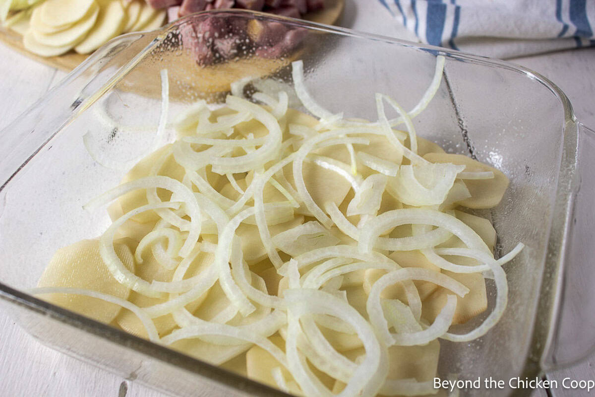 Sliced potatoes and onions in a casserole dish.