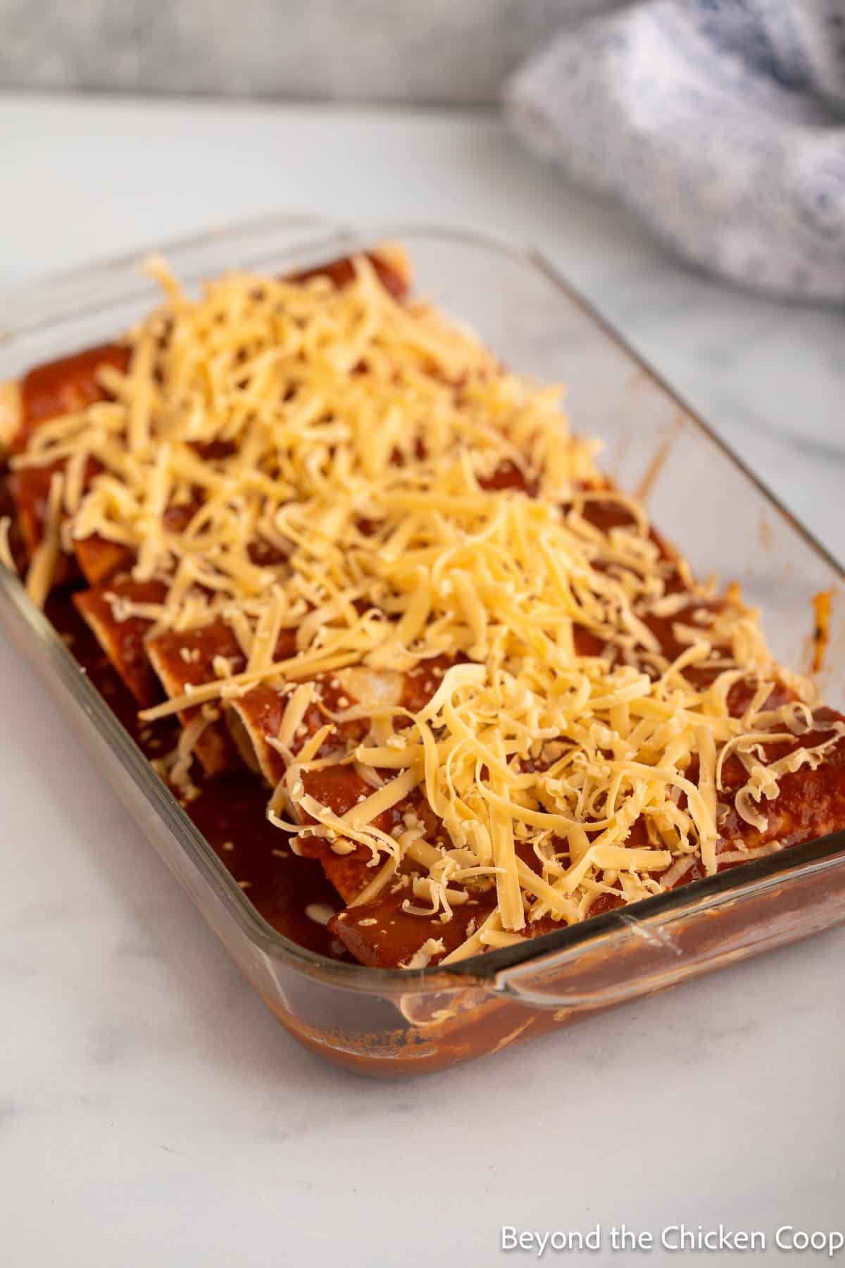 A dish filled with enchiladas topped with shredded cheese.