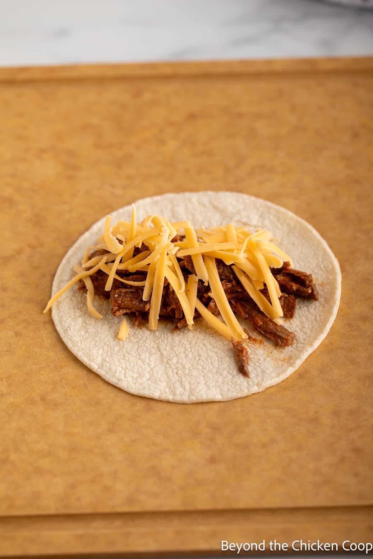 A tortilla topped with shredded beef and cheese.