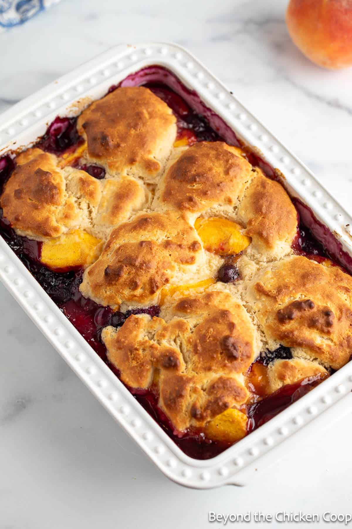 Cobbler with peaches and blueberries in a white baking dish.
