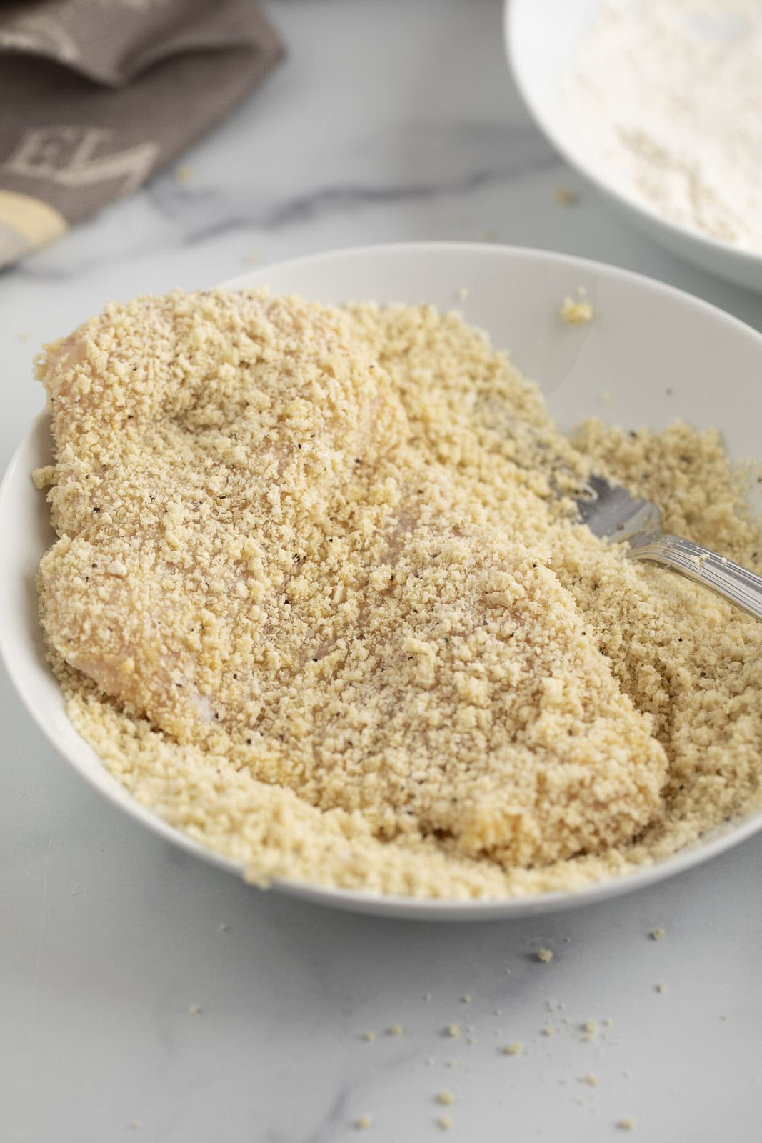 Dipping chicken into panko bread crumbs.