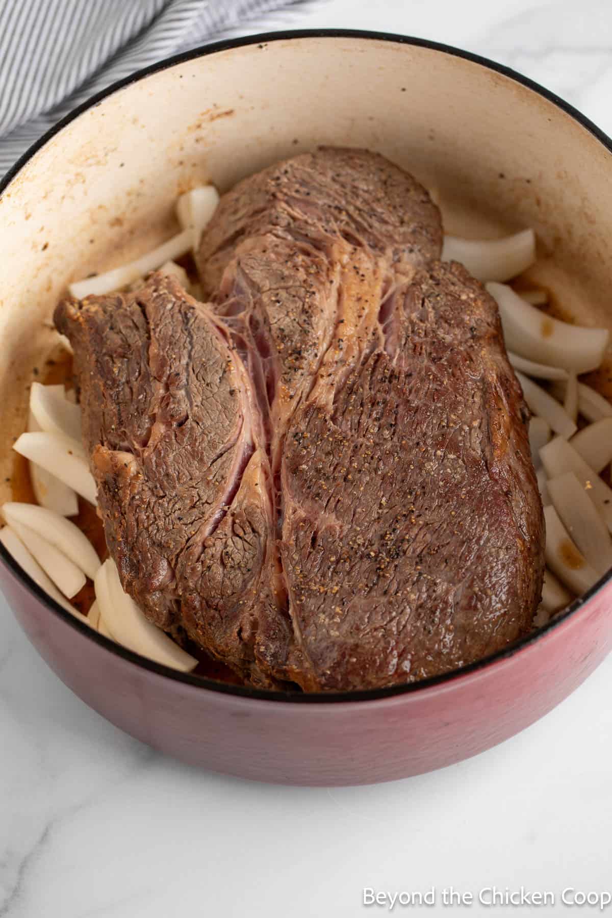 A browned chuck roast on top of sliced onions in a dutch oven.